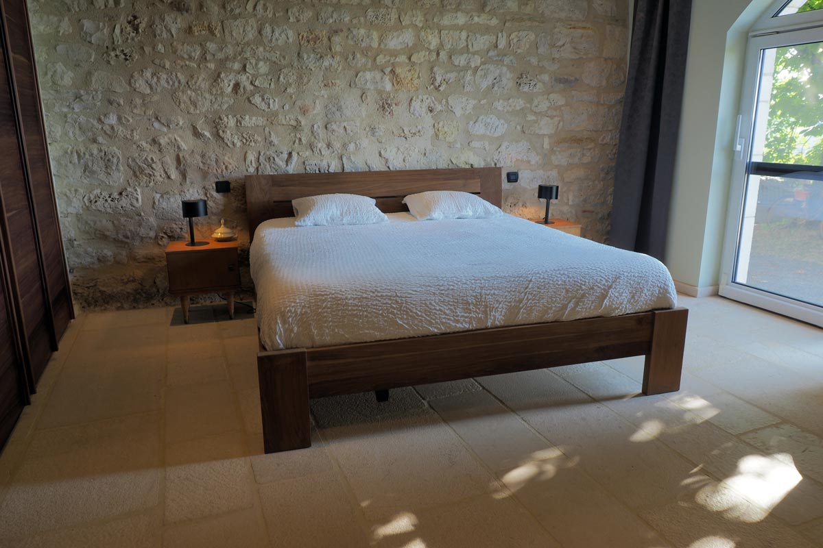 La chambre avec son mur en pierres, son grand lit confortable et de grands placards intégrés en palissandre.